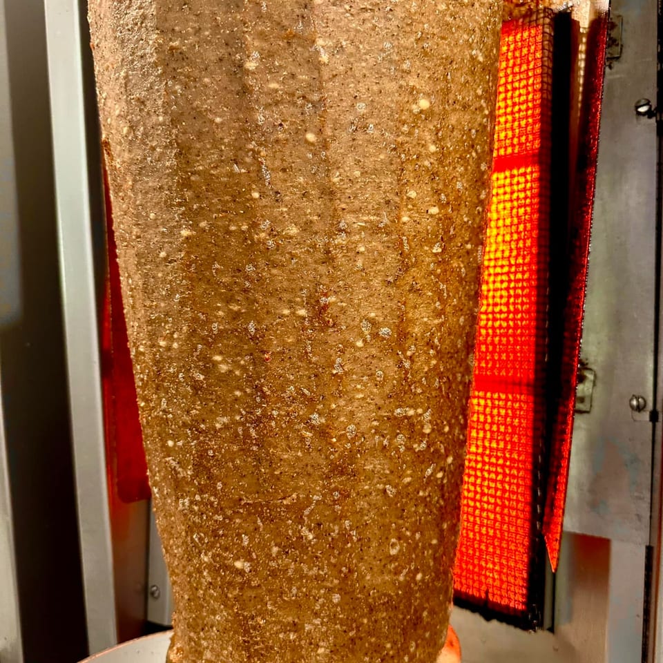 Gyro meat cone slowly roasting on a vertical spit next to a glowing red heating element.
