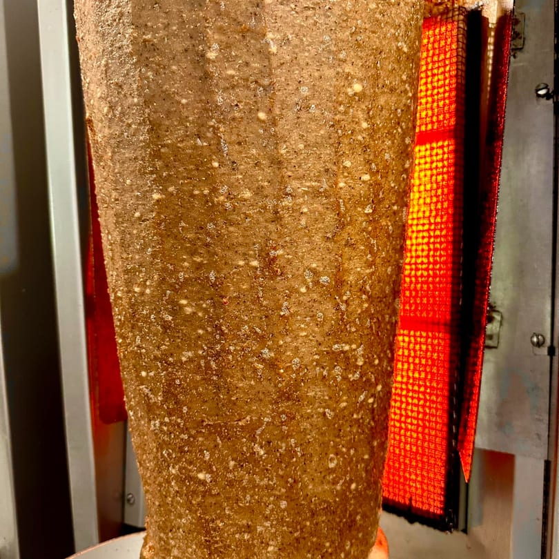 Gyro meat cone slowly roasting on a vertical spit next to a glowing red heating element.