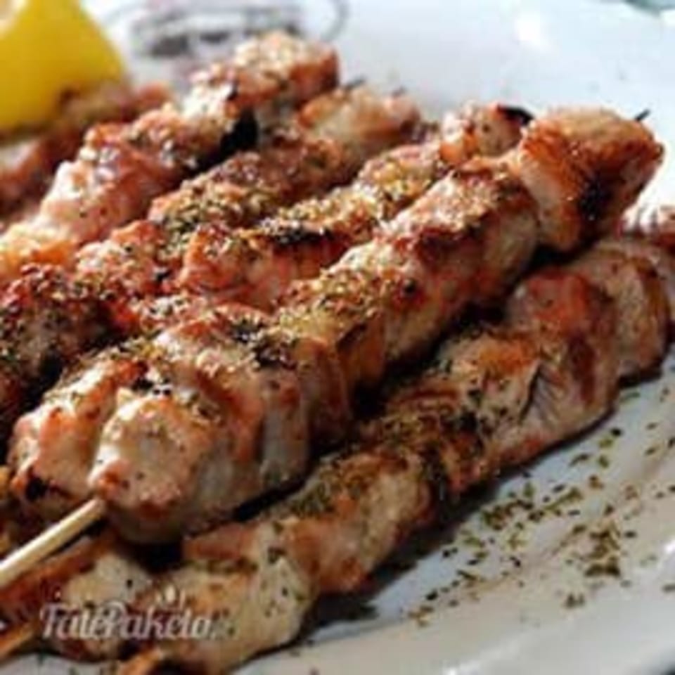 Close-up of several grilled chicken souvlaki skewers seasoned with herbs, served with a lemon wedge.