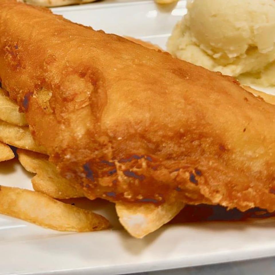 Golden-brown fried fish and thick-cut fries on a white plate, with a scoop of mashed potatoes.