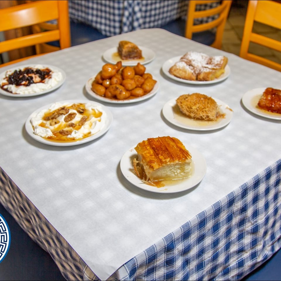 A table at Gyro House laden with various Greek desserts, including baklava, loukoumades, and yogurt with honey.