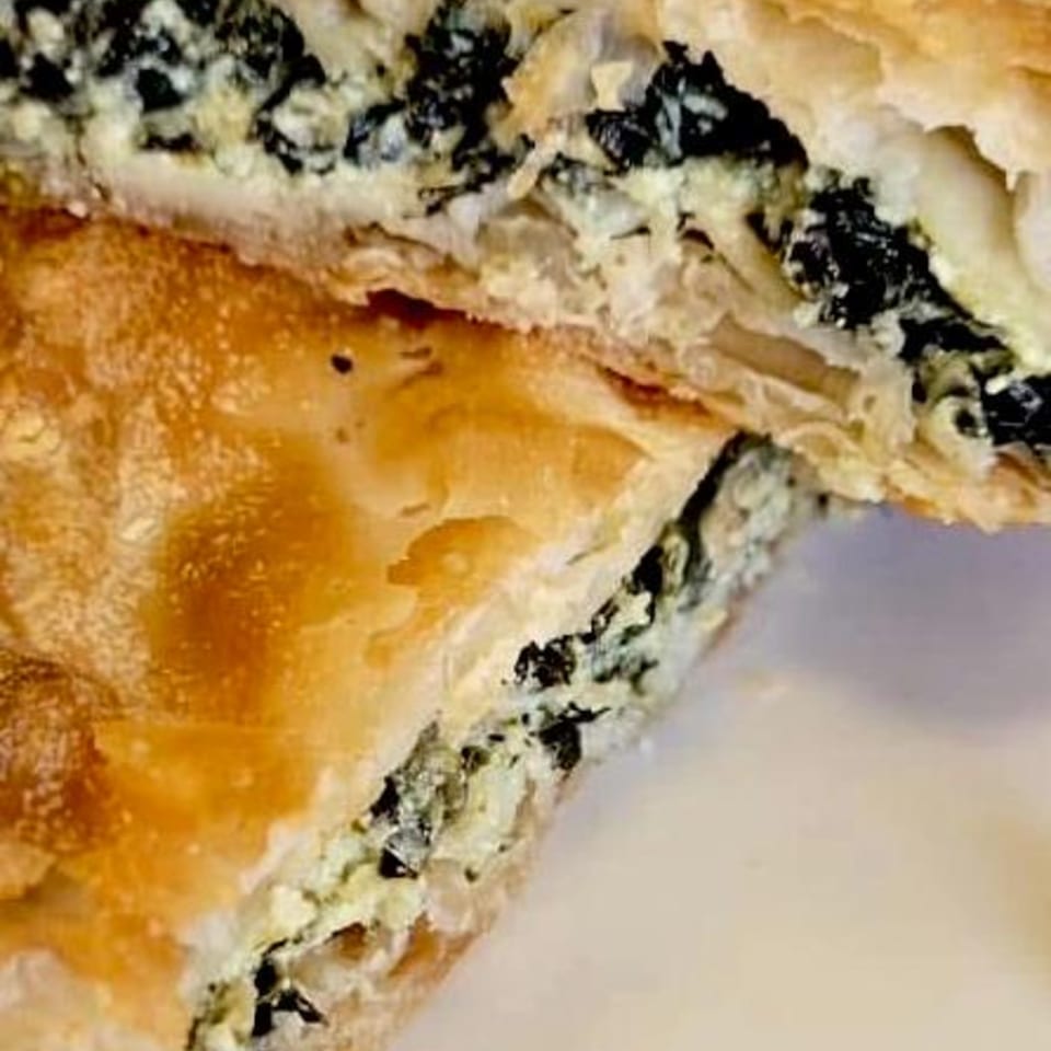 Close-up of a cut Greek spanakopita, revealing flaky pastry and a spinach and feta filling.