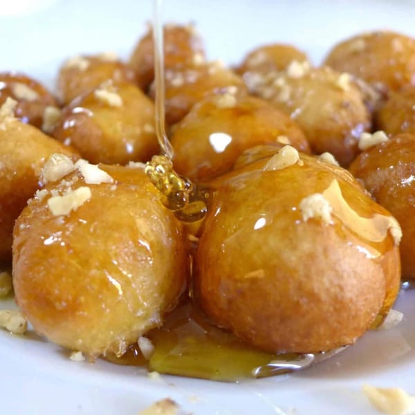 Golden Greek Loukoumades drizzled with honey and sprinkled with chopped nuts on a white plate.