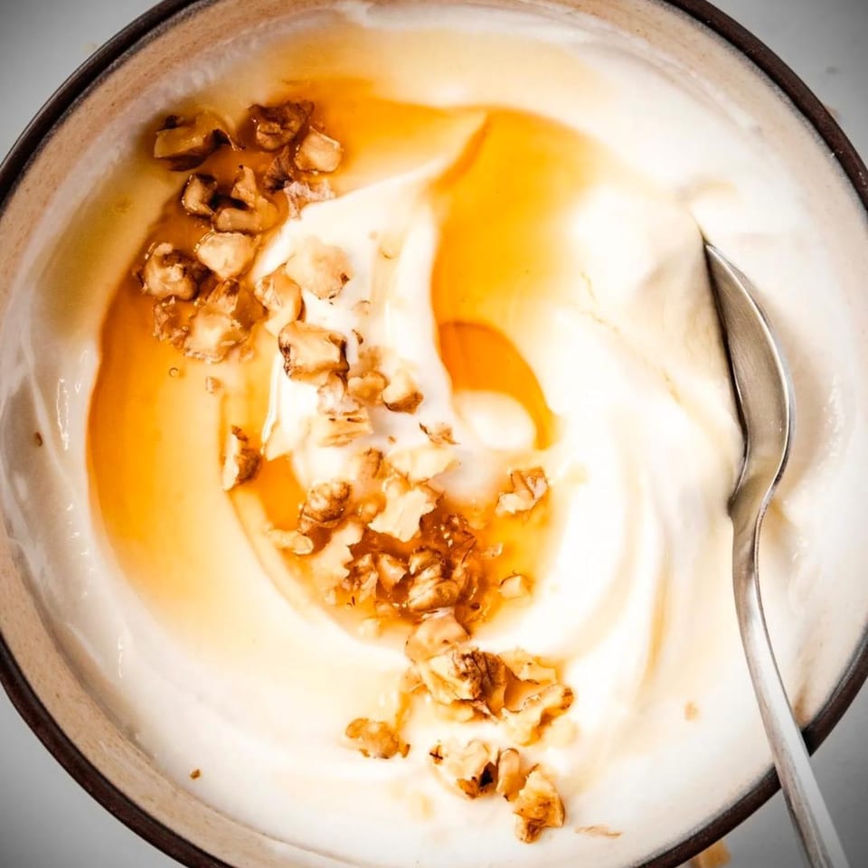 Overhead view of Greek yogurt with honey and walnuts in a bowl with a spoon.