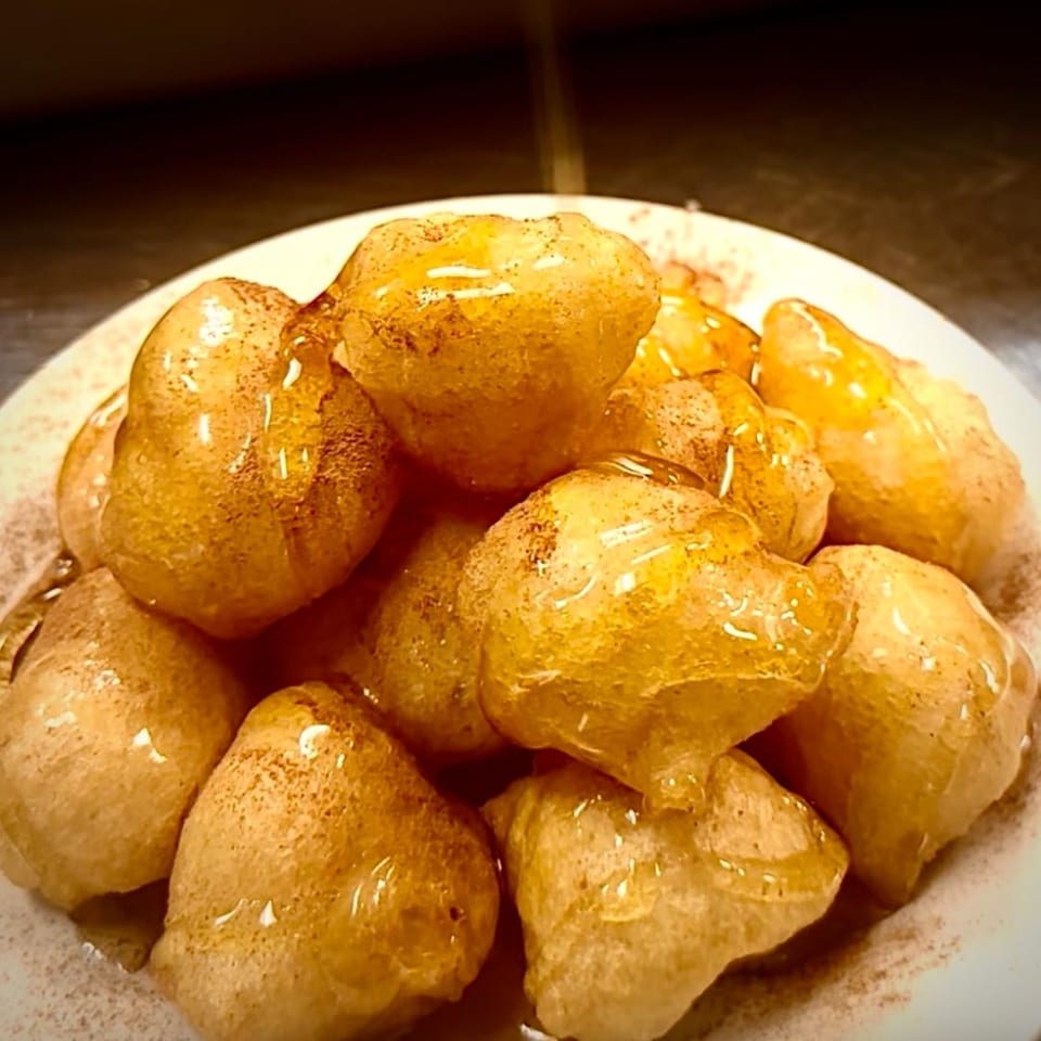 A close-up of golden-brown Greek Loukoumades, drizzled with honey and sprinkled with cinnamon.