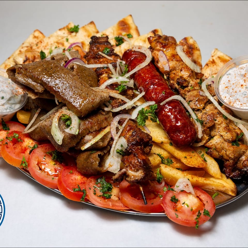 A large platter of Greek food with gyro meat, souvlaki, sausage, fries, pita, tomatoes, and tzatziki.