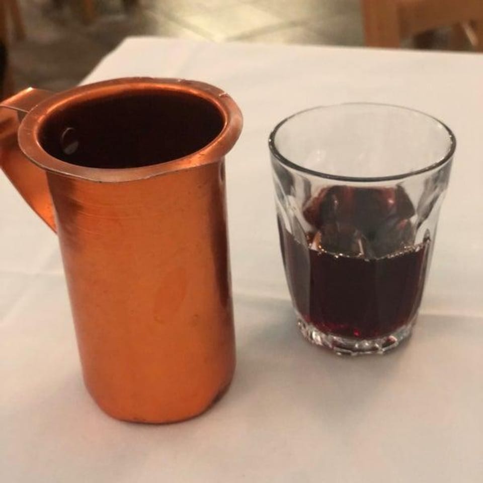 A copper pitcher and a glass of dark liquid, possibly coffee or wine, on a white tablecloth.
