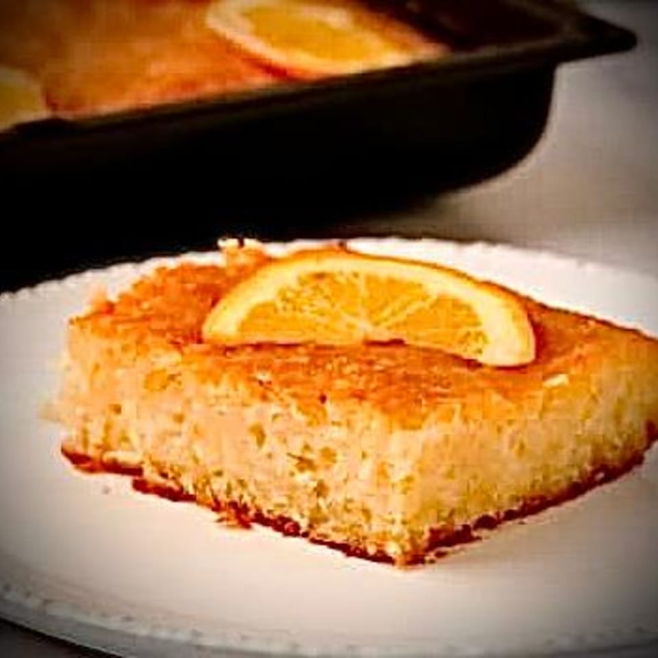 A slice of Greek orange cake, Portokalopita, topped with an orange slice on a white plate.