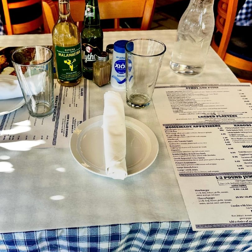 A Gyro House table set with Greek drinks, menus, and a white plate with a rolled napkin.