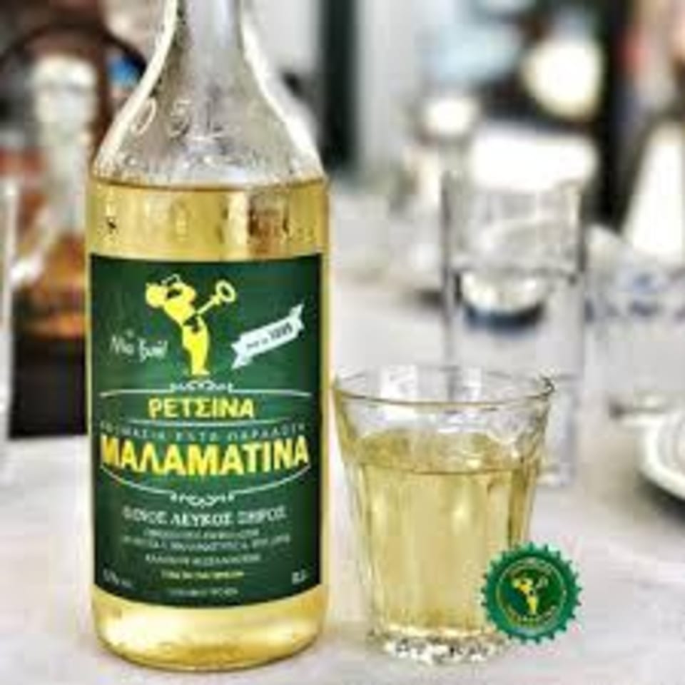 A bottle of Malamatina Retsina, a Greek white wine, next to a glass filled with the wine.