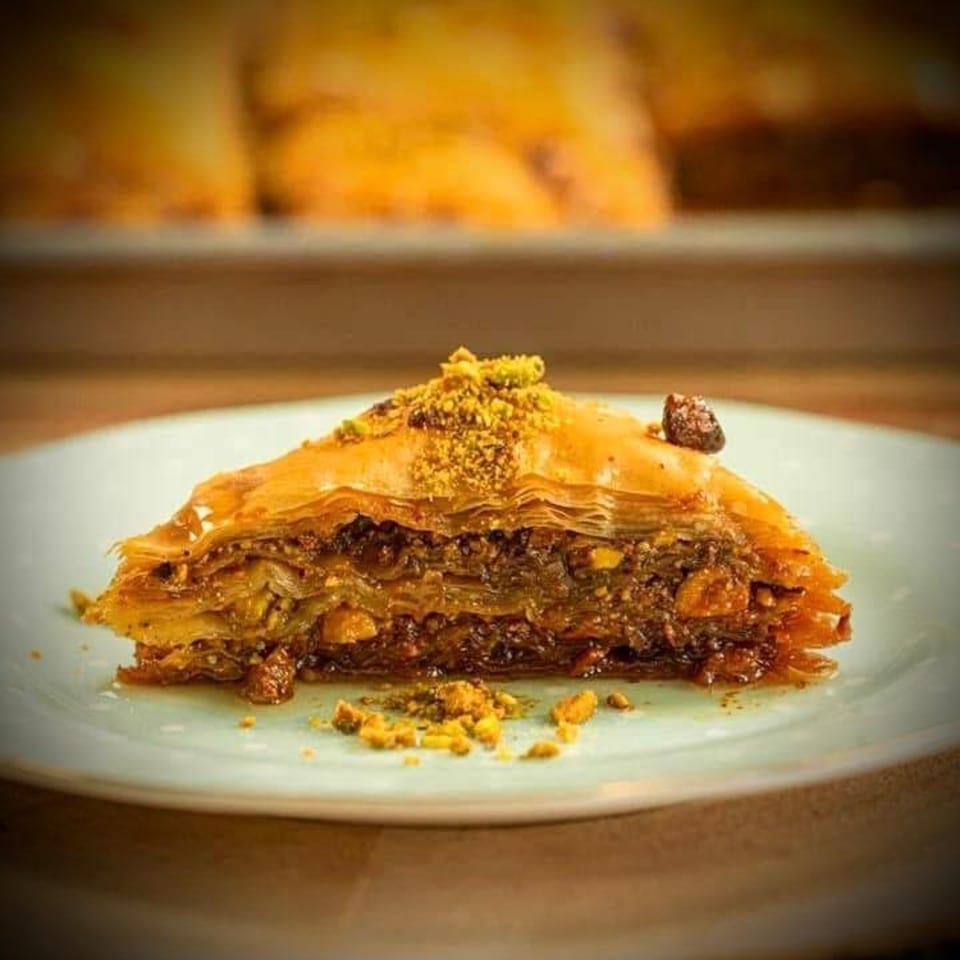 A slice of golden-brown baklava with layers of phyllo, nuts, and honey, topped with pistachios.